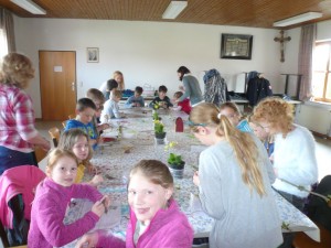 Die Kinder basteln an ihren Ketten bzw. Schlüsselanhängern. Die Schlüsselblumen stehen noch auf dem Tisch